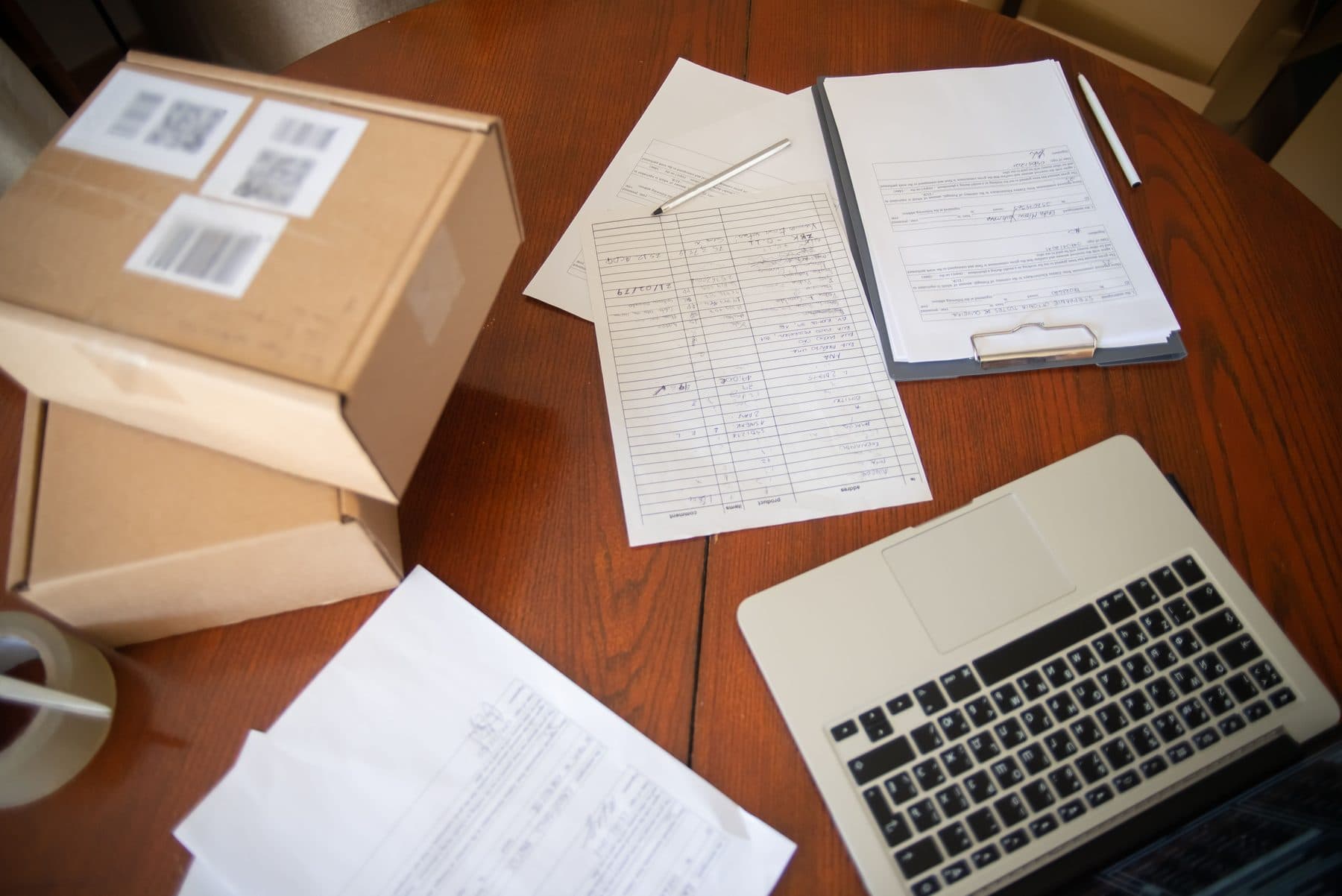 Overhead view of a table with a shipping box, handwritten order sheets, and an open laptop
