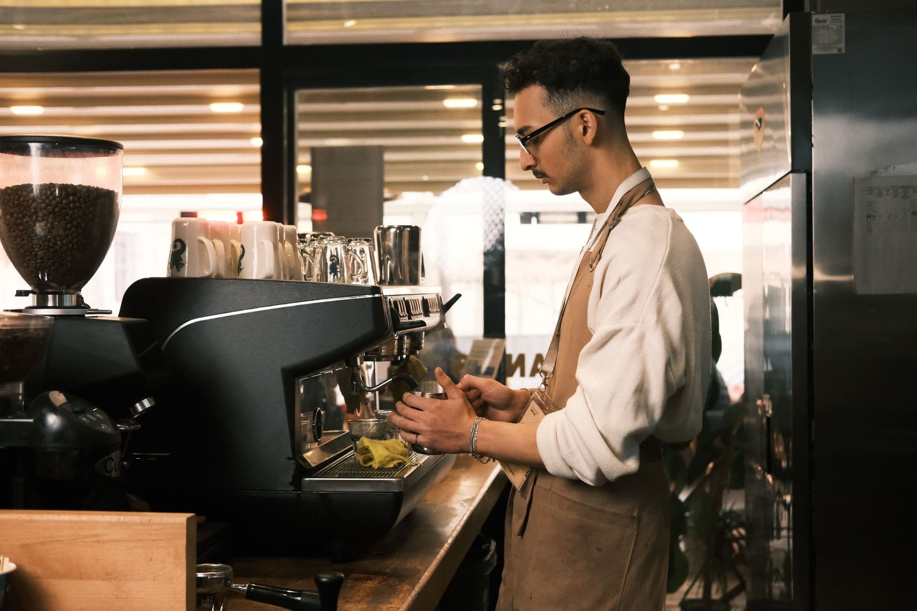Un barista prepara una bevanda dietro il bancone di un caffè dall'arredamento moderno, con tazze e attrezzature in vista