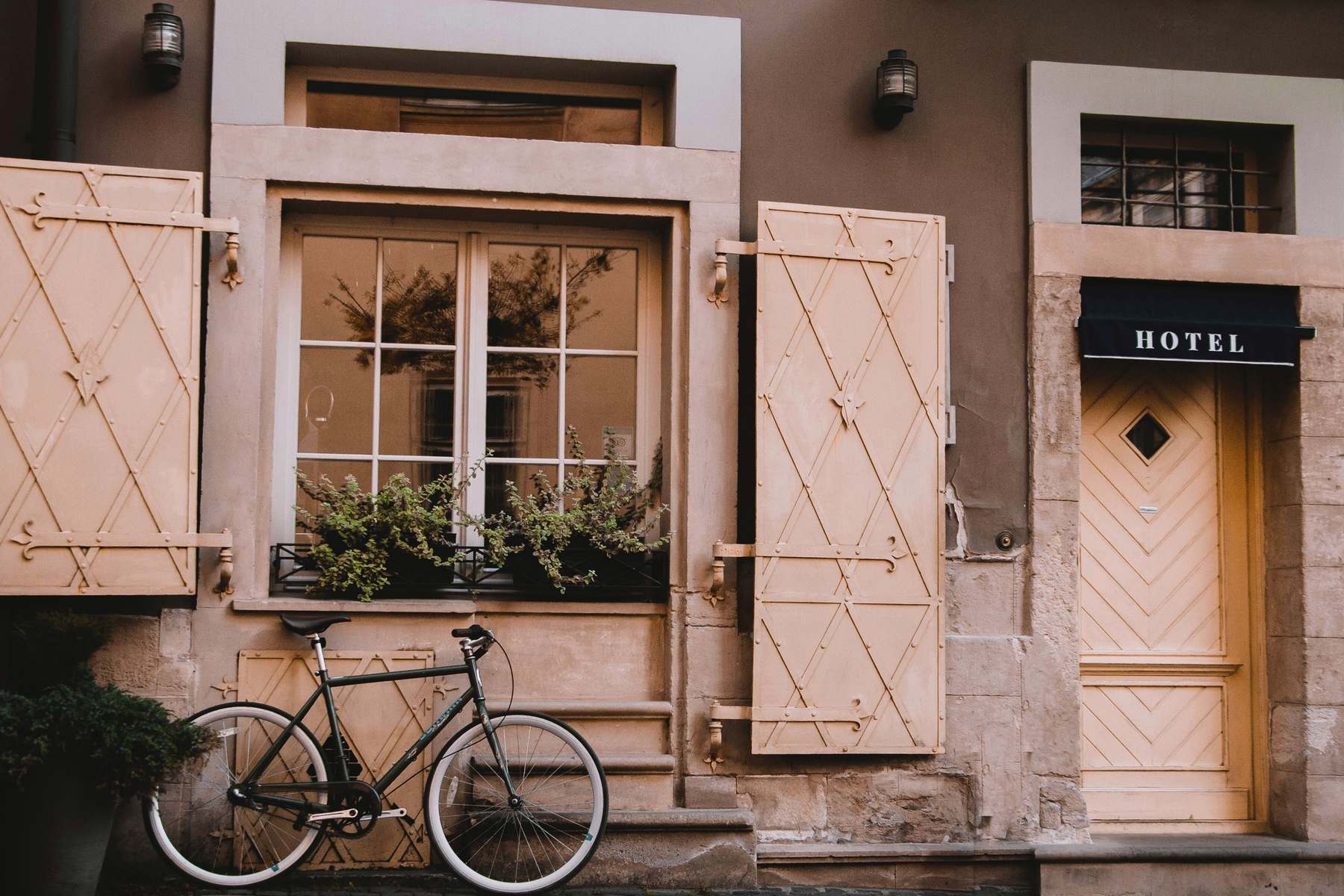 The cream-coloured facade of a small European hotel, with decorated shutters, a bicycle leaning against the wall, and a Hotel sign above the entrance door