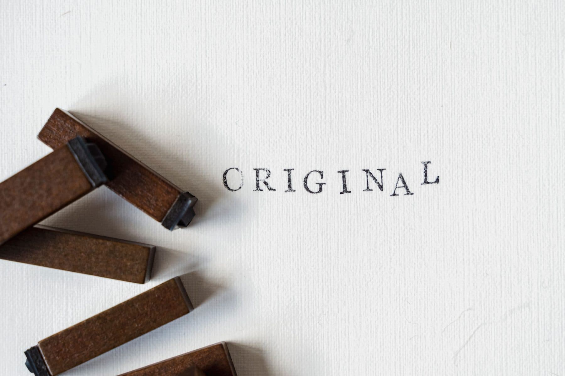 Wooden stamps printing the word ORIGINAL on a light sheet of paper, seen from above