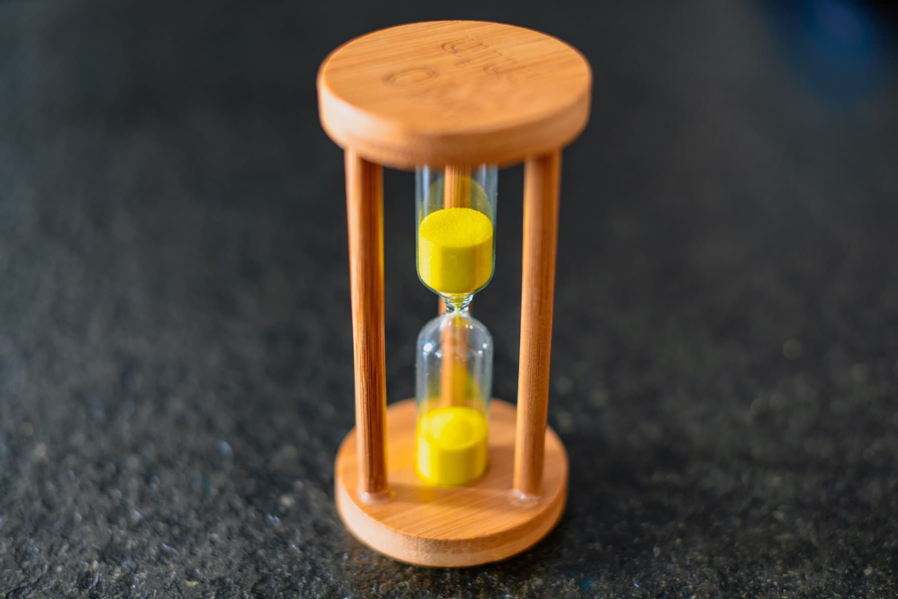 A wooden hourglass with yellow sand, close up against a dark surface