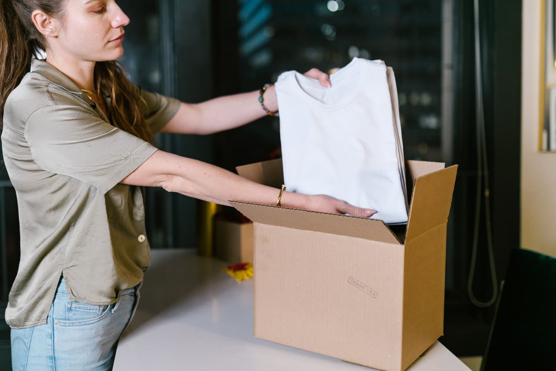 Open cardboard box on a table with a folded piece of clothing inside, ready to be shipped back as a return