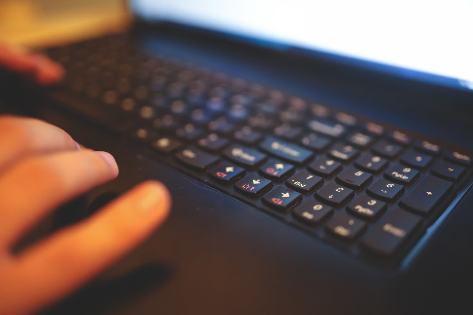 Close-up of a hand typing on a laptop keyboard, with the blurred, overexposed screen in the background