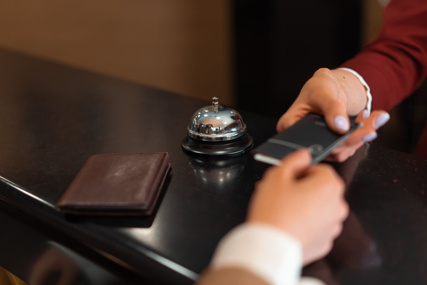 A guest hands over a wallet and a smartphone at a hotel front desk, next to the service bell