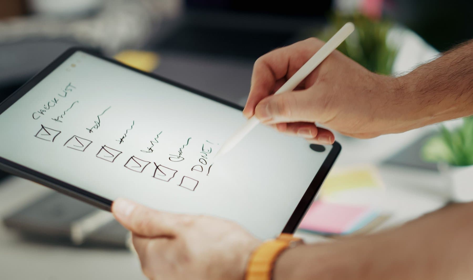 Mano che tiene uno stilo sopra un tablet, disegnando caselle da spuntare su una lista scritta a mano