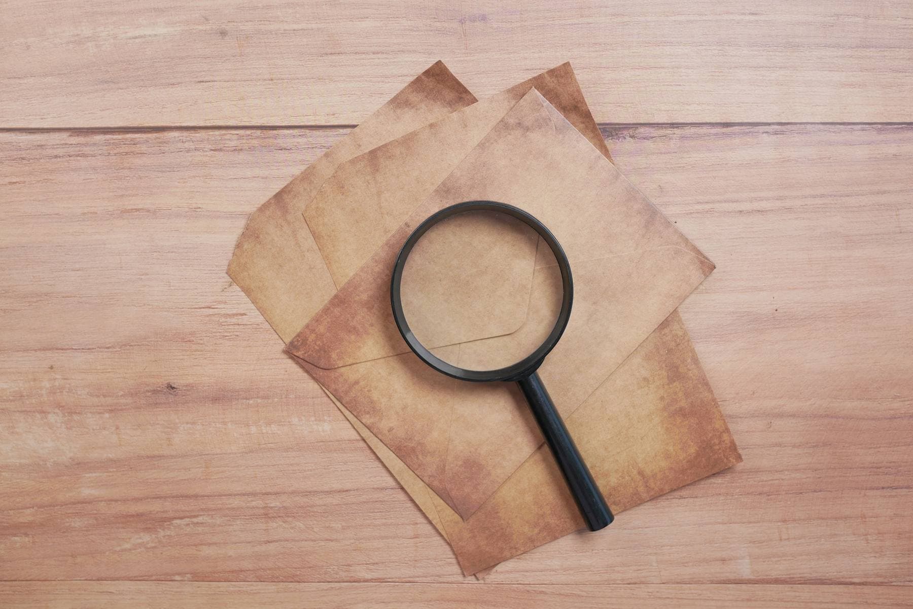 Una lente d'ingrandimento appoggiata su alcune vecchie buste da lettera, su un tavolo di legno chiaro