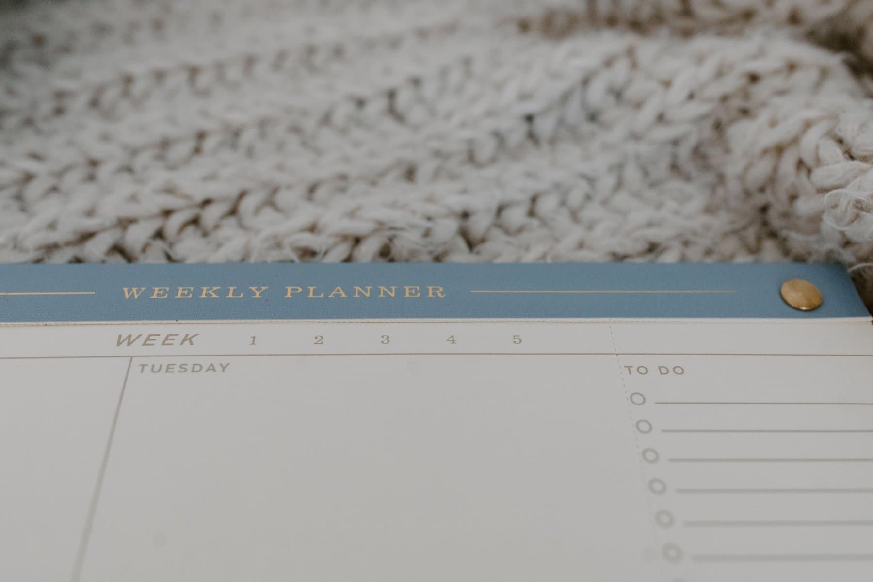 An open weekly planner on a page with boxes for each day and a to-do list, resting on a knitted wool blanket
