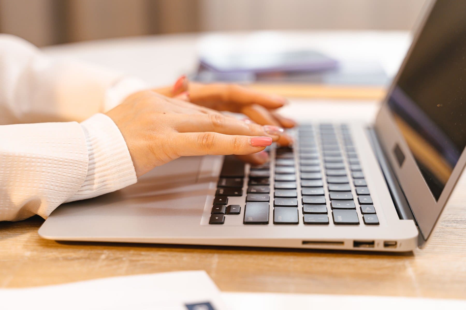 Close-up of hands typing on a laptop keyboard at a light wooden desk