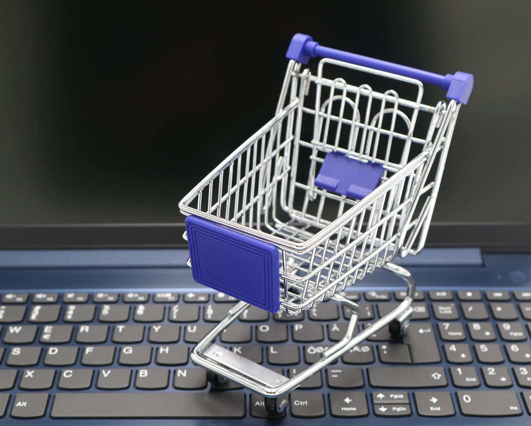 Un carrello della spesa in miniatura, con le ruote, appoggiato sulla tastiera di un computer portatile