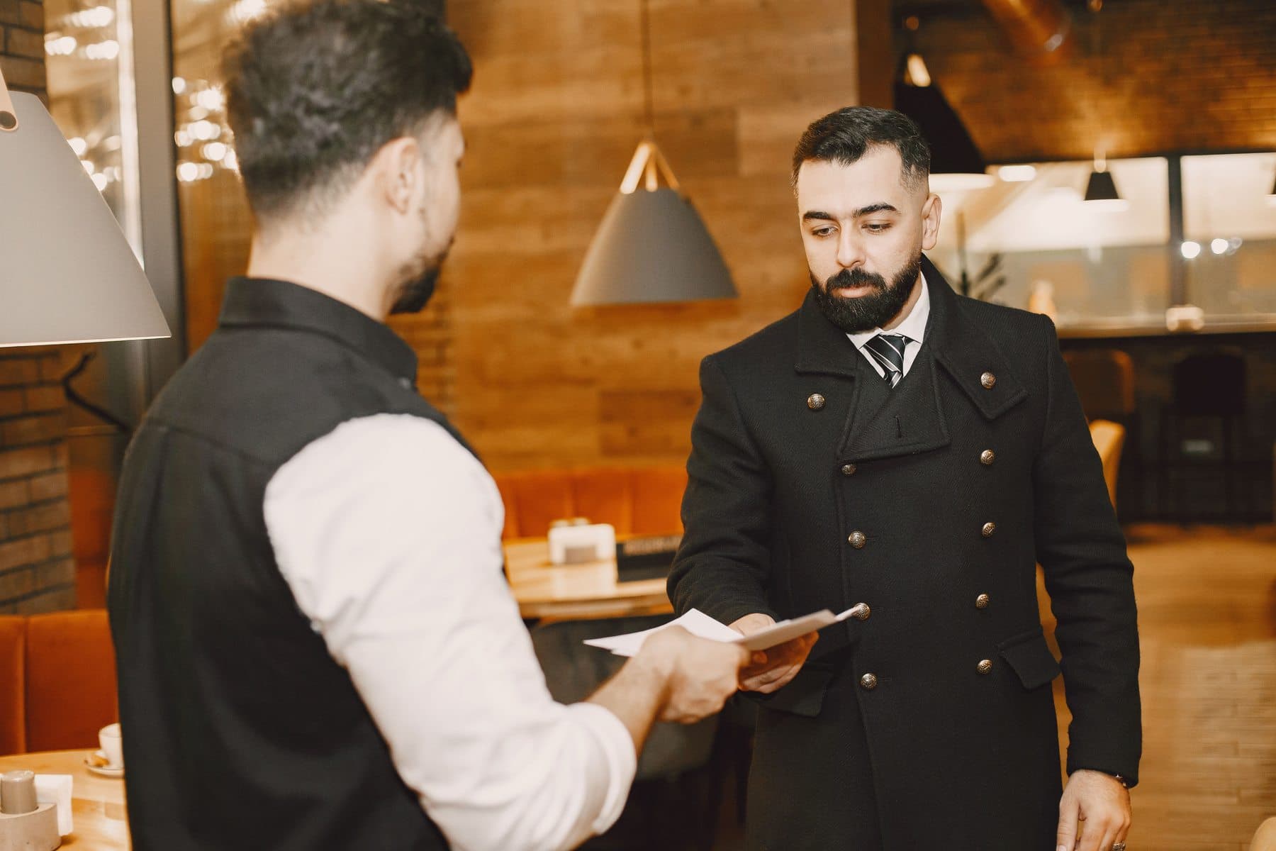Un cameriere consegna un menu a un cliente in piedi, in un ristorante dall'arredamento caldo in legno