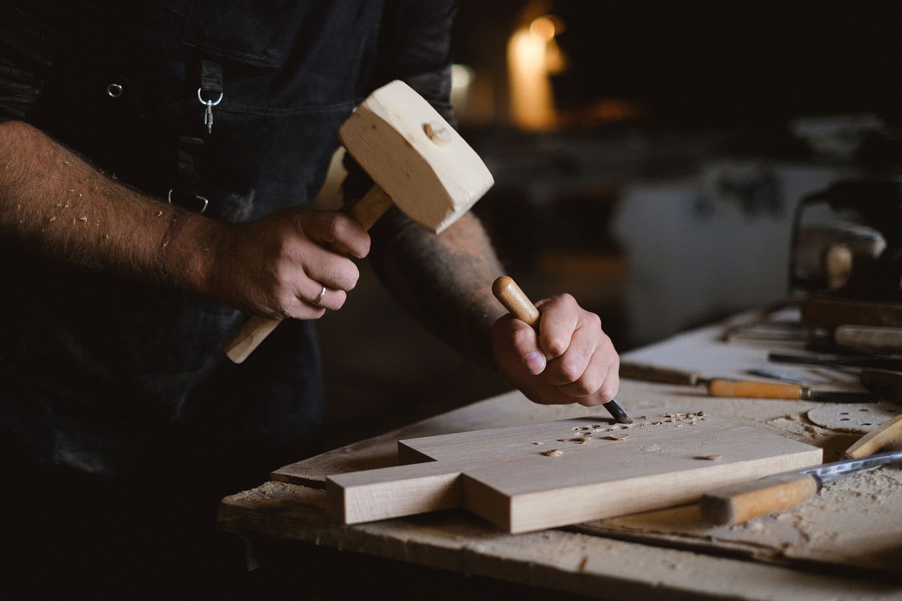 Le mani di un artigiano al lavoro su un pezzo di legno con degli scalpelli, su un banco da lavoro