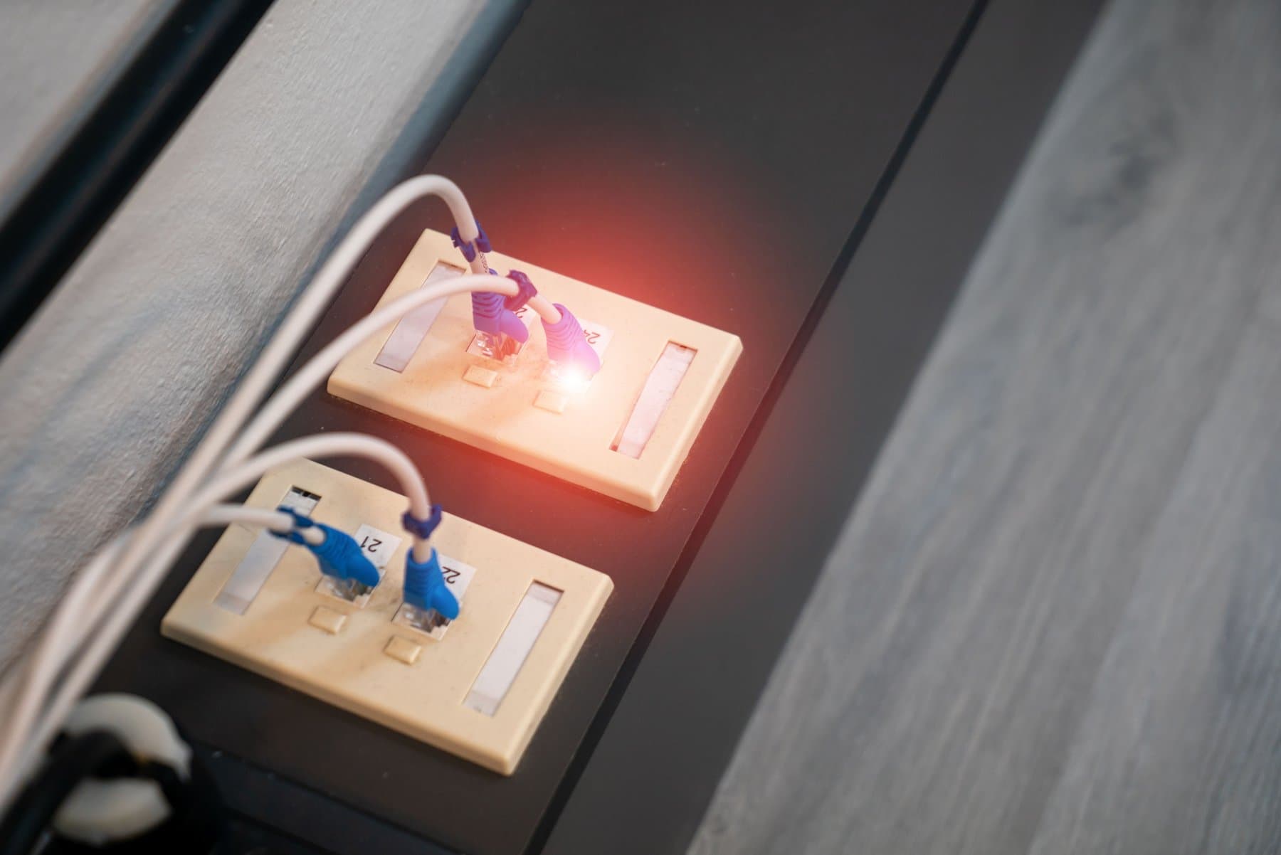 Close-up view of two wall network sockets with ethernet cables plugged in and a lit indicator light