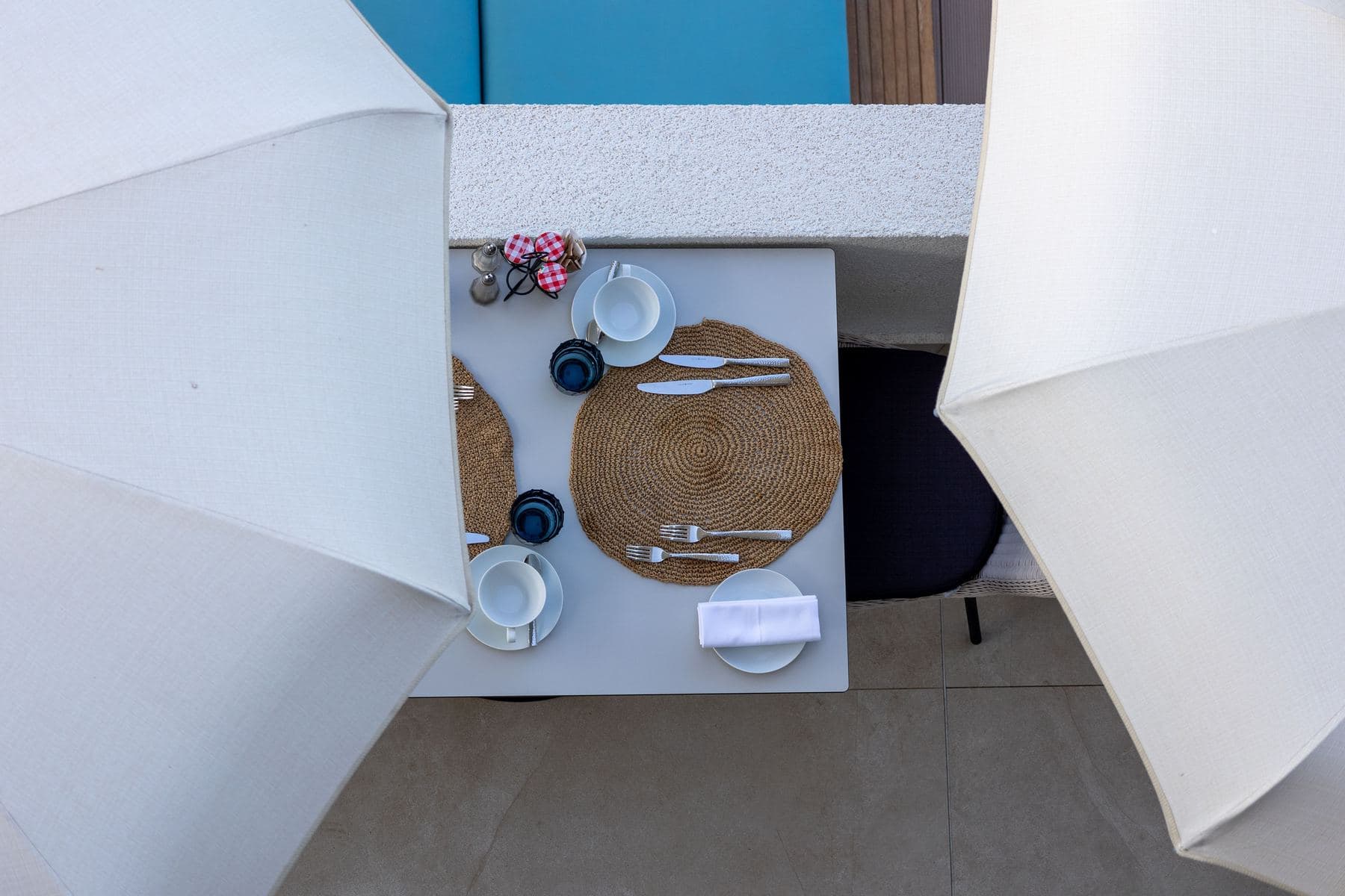 Overhead view of an elegant table set for two on a terrace, between two white umbrellas